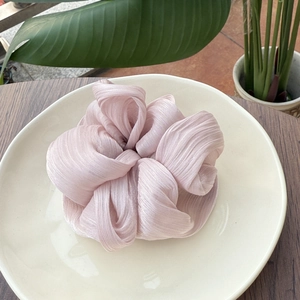 Chouchou en satin plissé rose pâle à texture florale sur une assiette en céramique