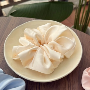 Chouchou géant élégant en satin de soie crème sur assiette avec feuilles vertes
