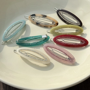 Detailed macro view of oval rhinestone hair clips in various colors on a ceramic plate