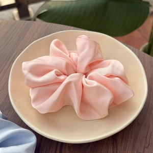 Chouchou élégant en satin de soie rose pâle sur une assiette en céramique et fond en bois