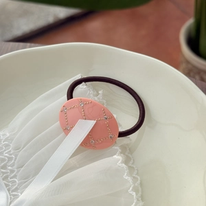 Pink oval acetate hair tie with rhinestone inlay and grid pattern on white lace