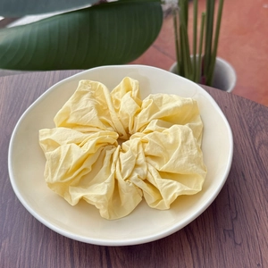 Soft pale yellow scrunchie with pleated texture placed on a white ceramic plate