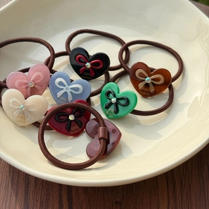 Detailed macro view of acetate heart-shaped hair ties with rhinestone bow on a ceramic plate