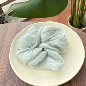 Gros plan du chouchou plissé vert menthe avec reflet soyeux sur une assiette blanche