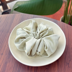 Détail d'un chouchou en soie vert clair sur une assiette décorative avec fond esthétique