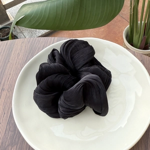 Détail de la texture d'un chouchou plissé noir posé sur un plateau en céramique blanc