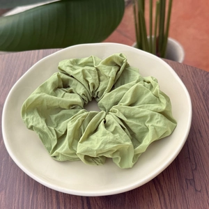 Close-up of grass green scrunchie with soft pleated texture on a white ceramic plate