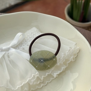 Macro detail of oval acetate hair tie with olive green resin and sparkling rhinestones