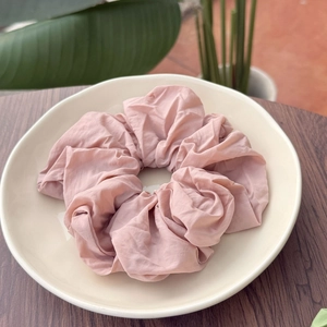 Detail of soft matte lotus pink fabric scrunchie on beige ceramic plate display