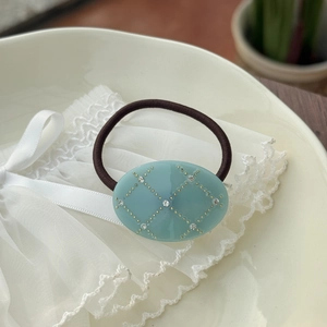 Detail of elegant blue oval resin hair tie with gold grid pattern and rhinestones