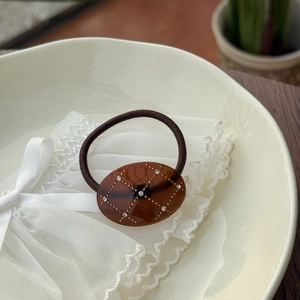 Detail of an oval amber acetate hair tie with gold grid patterns and crystal rhinestones