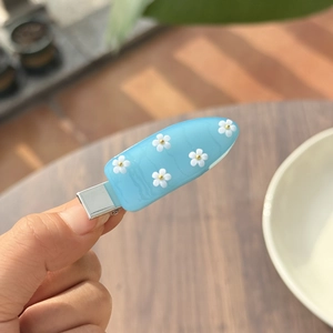 Gedetailleerde close-up van een lichtblauwe acryl haarspeld met witte 3D bloemmotieven