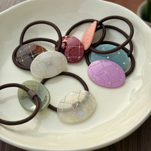 Detailed view of colorful oval hair ties with quilted patterns and crystals in a ceramic tray