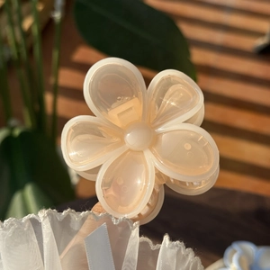 Close-up of a translucent peach flower hair claw clip held by hand in natural sunlight
