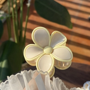 Close-up of a jelly floral hair claw clip in creamy yellow on a rustic wood background