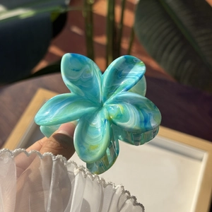Pinza per capelli a fiore con motivo marmorizzato blu tenuta in mano con luce naturale