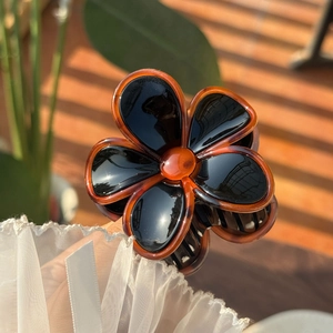 Close-up of a floral hair claw clip in amber and black finish with glossy resin details