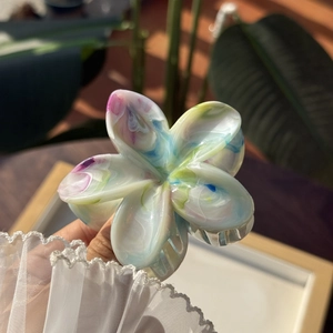 Dettaglio macro della molletta per capelli a forma di plumeria con motivi marmorizzati a inchiostro