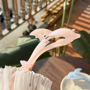 Macro detail of a pearlescent pink dolphin-shaped hair claw clip with a glossy finish
