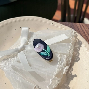 Détail d'une pince à cheveux tulipe en acétate avec fleur violette et perle sur dentelle