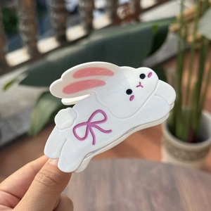 Close-up of cute white acetate rabbit hair claw clip with pink bow held by a hand outdoors