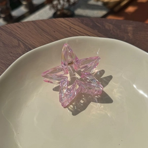 Iridescent pink star hair claw clip made of clear resin with gold spring on a plate