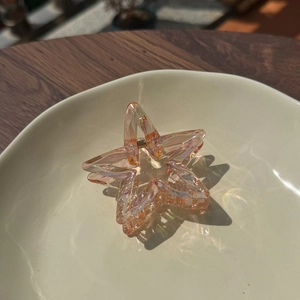 Translucent orange star-shaped hair claw clip with iridescent finish and metal spring