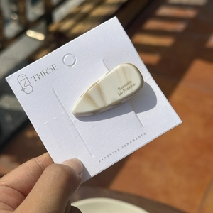Barrette en acétate beige marbré avec logo doré sur carte de présentation