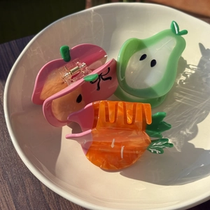 Detailed view of apple pear and carrot shaped acetate hair claws in a white ceramic dish