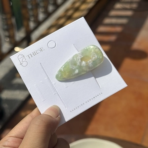 Gros plan d'une pince à cheveux en acétate marbré vert clair sur carte de marque
