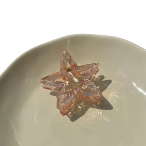 Pink translucent star hair claw clip with colorful iridescent finish on ceramic plate
