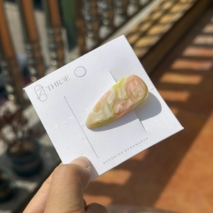 Gros plan d'une pince à cheveux en acétate marbré rose et vert sur carte blanche