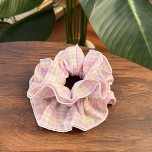 Plaid fabric scrunchie with pink yellow patterns and white stitching on a wooden table