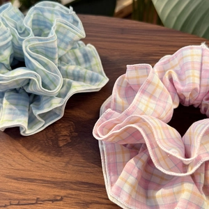 Close-up of plaid fabric scrunchies in blue-green and pink-yellow with detailed white edges
