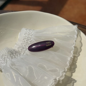 Detail of purple acetate hair clip with gold engraving on elegant white lace texture