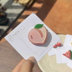 Pink peach shaped acetate hair clip with green leaf and rhinestone detail on card