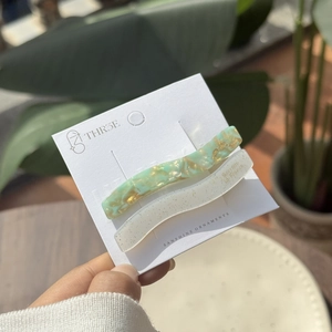 Detail of two wavy hair clips in marble green and glittery resin on display card