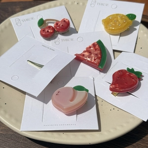 Detail shot of fruit-shaped acetate hair clips with rhinestones on a display card
