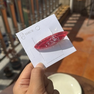 Détail de la pince à cheveux ovale en résine rouge pailletée avec des éclats d'argent