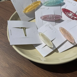 Détail de barrettes à cheveux ovales en résine colorée avec paillettes et plat