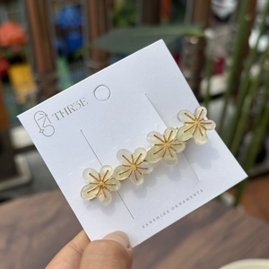 Nahaufnahme von vier Acetat-Blumen-Haarspangen mit Goldfaden auf einer Geschenkkarte