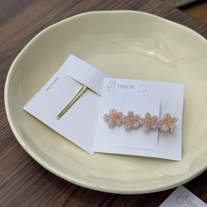 Detail einer Haarspange mit rosa Acetatblüten und Golddraht auf einer Keramikplatte