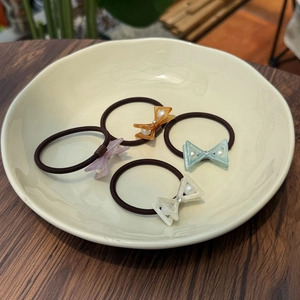Close-up of four bow hair ties with pearls and rhinestones in a cream-colored dish