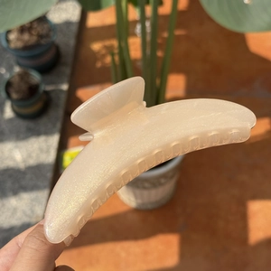 Close-up of a large moon-shaped hair claw clip in pearlescent pink under natural sunlight