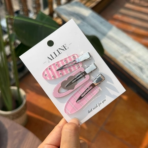 Dettaglio di tre mollette per capelli in acrilico rosa con motivi a cuore e righe