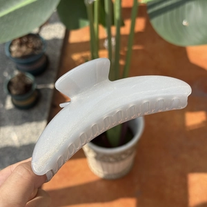 Close-up of a pearlescent white moon hair claw with glitter finish in outdoor sunlight