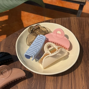 Close-up of assorted pastel hair claws in a ceramic bowl on a wooden table surface