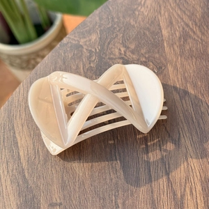 Elegant beige X-shaped cross hair claw clip with glossy finish on a dark wooden surface