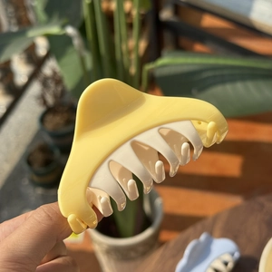 Minimalist yellow and cream plastic claw clip for hair styling in natural sunlight