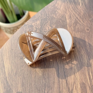 Elegant X-shaped amber and cream resin hair claw clip displayed on a wooden surface